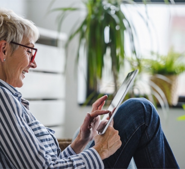 Eine Frau in einem getsreiften Hemd sitz an der Wand lehnend auf dem Boden und schaut auf ein Tablet,